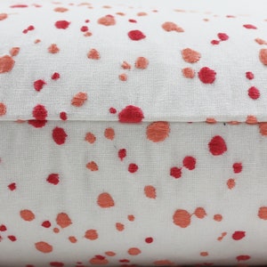 Op de afbeelding: Close-up van een wit kussen met een rood en oranje splatterpatroon. Het kussen heeft een naad in het midden.