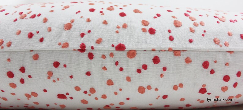 Op de afbeelding: Close-up van een wit kussen met een rood en oranje splatterpatroon. Het kussen heeft een naad in het midden.