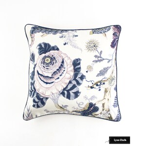 May include: A white pillow with a navy blue trim features a floral pattern with large pink and white flowers and smaller yellow flowers. The background is a cream color.
