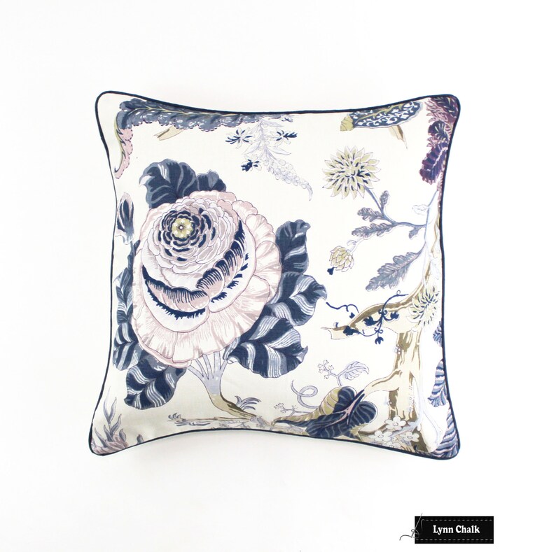 May include: A white pillow with a navy blue trim features a floral pattern with large pink and white flowers and smaller yellow flowers. The background is a cream color.