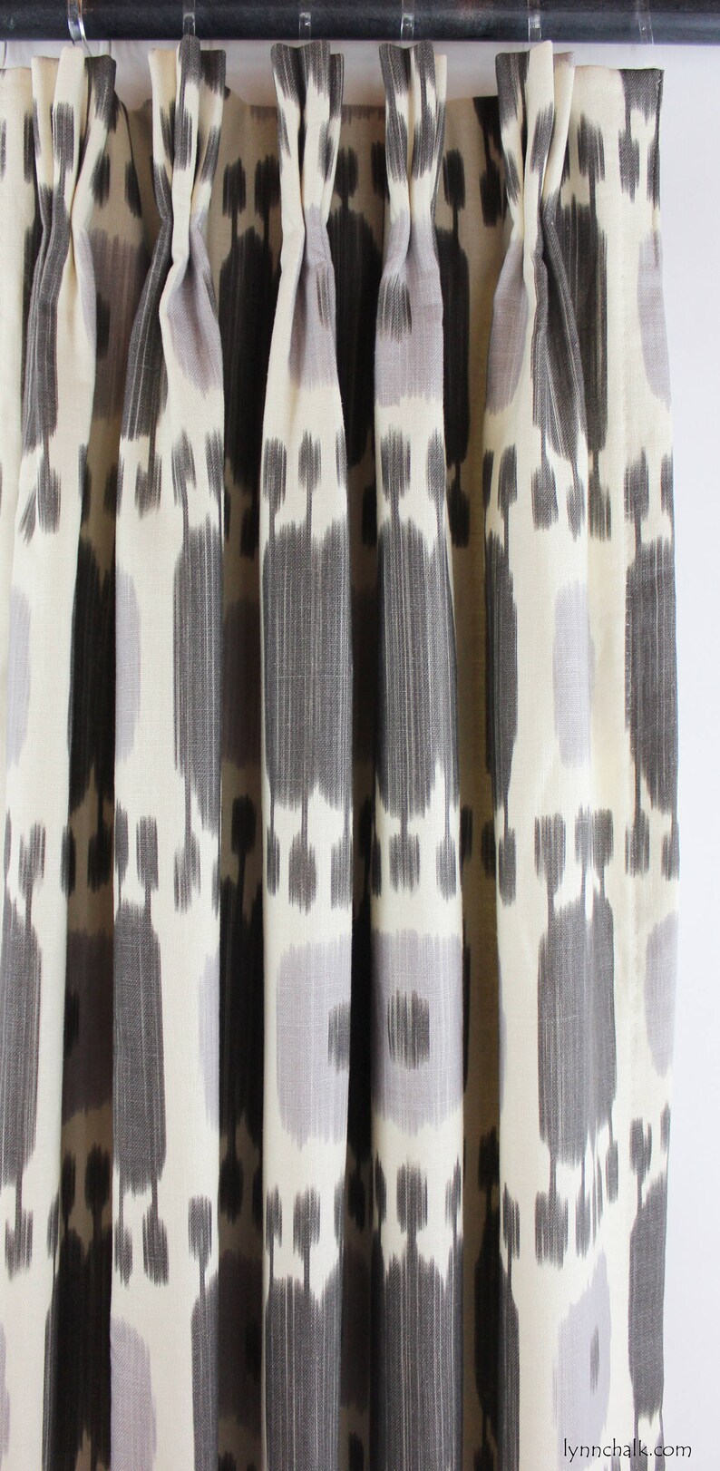 May include: Close-up of a set of gray and white patterned curtains with a geometric design. The curtains are pleated and hung on a black rod.