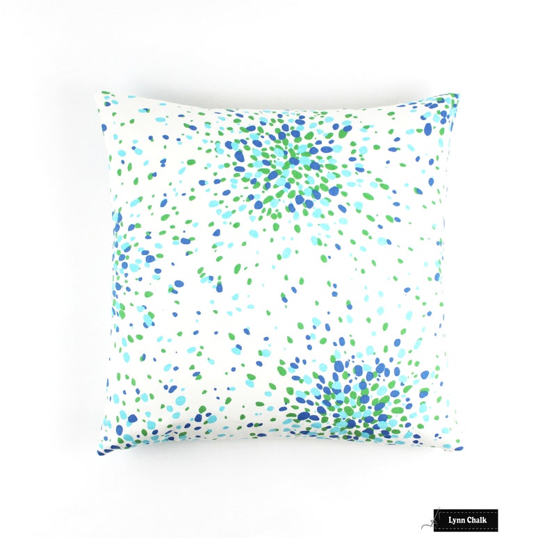 May include: A white cushion with a blue and green confetti pattern. The cushion is square and has a white background.
