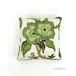 May include: A white pillow with a green floral pattern. The pillow features two large green flowers with dark green centers and leaves. The background is a light cream color.