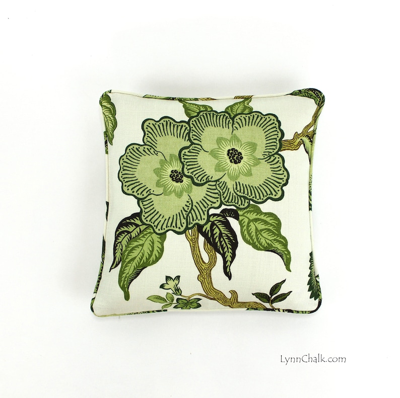May include: A white pillow with a green floral pattern. The pillow features two large green flowers with dark green centers and leaves. The background is a light cream color.