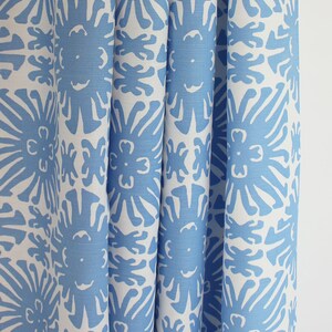 May include: Close-up of a white fabric with a blue floral pattern. The fabric has a repeating pattern of stylized flowers with a sunburst design.