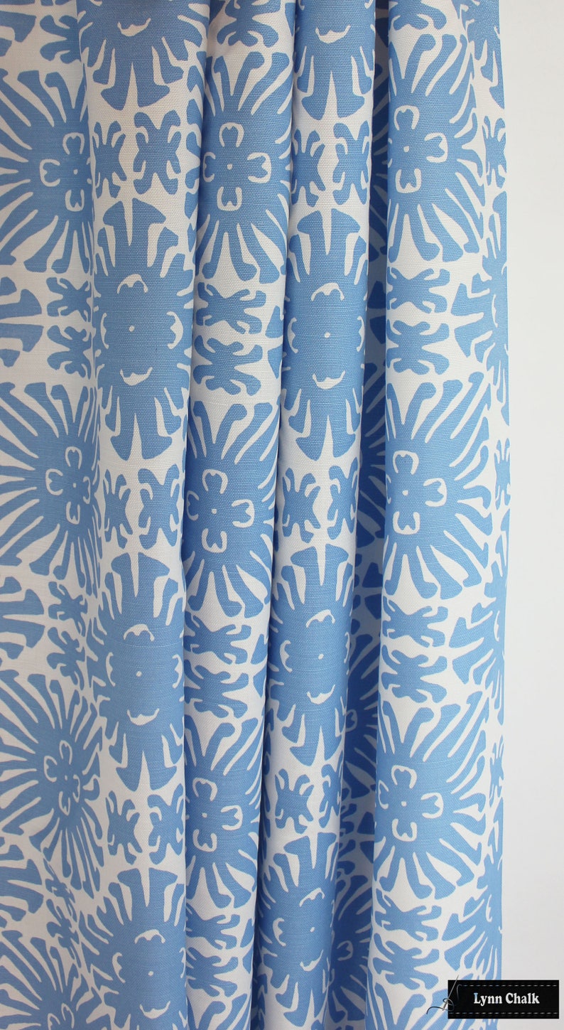 May include: Close-up of a white fabric with a blue floral pattern. The fabric has a repeating pattern of stylized flowers with a sunburst design.
