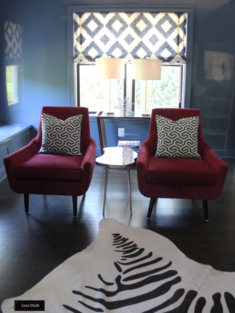 May include: Two red velvet armchairs with black and white patterned cushions sit in front of a window with a black and white patterned valance. A zebra print rug is on the floor in front of the chairs.