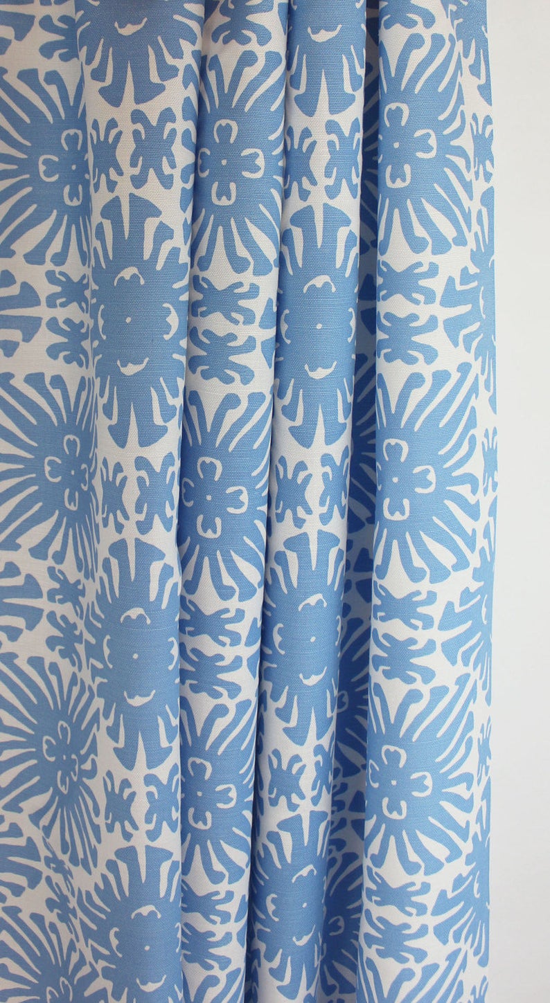 Puede incluir: Cortinas estampadas en azul y blanco. La tela presenta un dise&ntilde;o floral repetitivo en azul claro sobre un fondo blanco. Las cortinas est&aacute;n dobladas, mostrando la textura y el patr&oacute;n de la tela. El tema general es la decoraci&oacute;n del hogar.