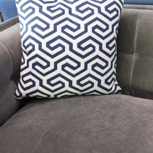 May include: A white and navy blue geometric patterned throw pillow. The pillow is on a gray couch.