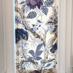 May include: A white window with a floral patterned roman shade. The shade features a large, dark blue and purple flower with a white background. The window is trimmed in white molding.