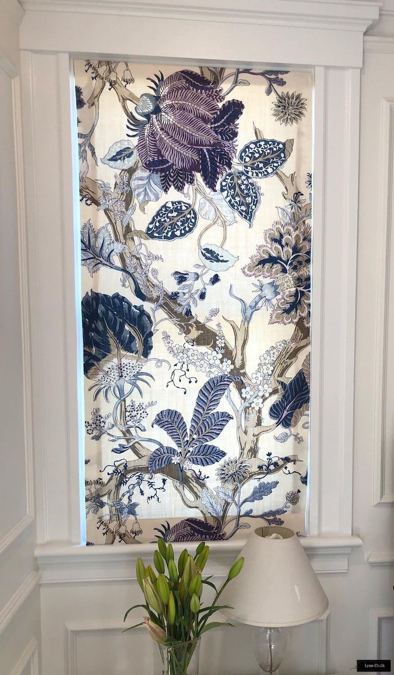 May include: A white window with a floral patterned roman shade. The shade features a large, dark blue and purple flower with a white background. The window is trimmed in white molding.