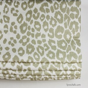 May include: A white fabric roman blind with a beige leopard print pattern. The blind is folded up, showing the layers of fabric.