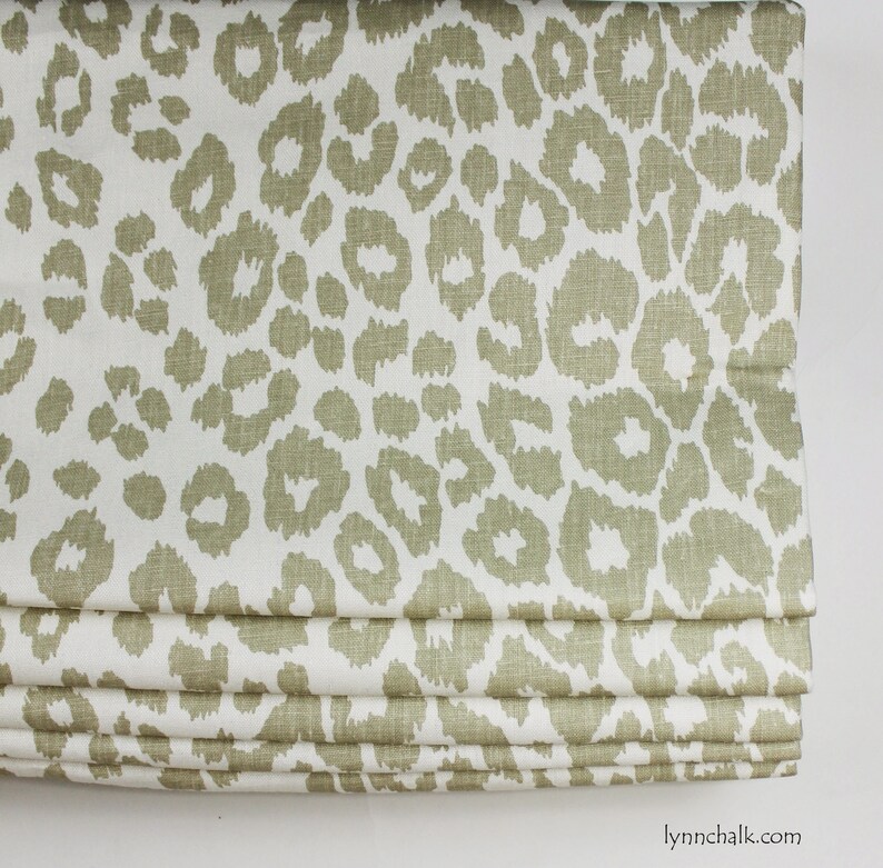 May include: A white fabric roman blind with a beige leopard print pattern. The blind is folded up, showing the layers of fabric.