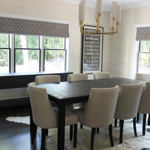 May include: A black dining table with six chairs, a black console table, and a black and white patterned valance. The table is set with a white tablecloth and a white rug. The room has white walls and a black floor. A framed print with the text "OPER NOTRE-DAME MUSEED ORSAY CONCORDE CHAMPS-ELYSEES ROMPRE TROCADERO TOUR EIFFEL VALIDES" hangs on the wall.