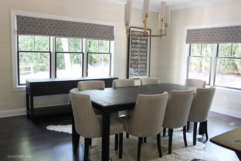 May include: A black dining table with six chairs, a black console table, and a black and white patterned valance. The table is set with a white tablecloth and a white rug. The room has white walls and a black floor. A framed print with the text "OPER NOTRE-DAME MUSEED ORSAY CONCORDE CHAMPS-ELYSEES ROMPRE TROCADERO TOUR EIFFEL VALIDES" hangs on the wall.