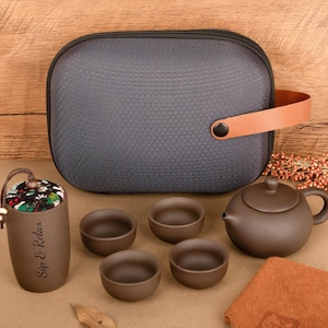 May include: A brown tea set comprising a teapot, four small cups, and a grey carrying case with a brown handle. A small cup with the text "Sip & Relax" is also included.