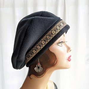 Puede incluir: Un gorro de lana negro con un borde de patr&oacute;n dorado y negro. El gorro se lleva en un maniqu&iacute; con un collar de perlas y pendientes.