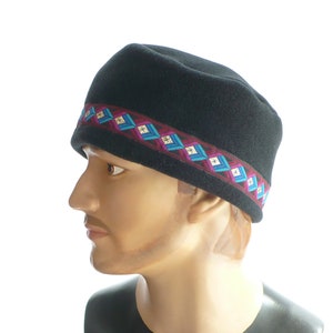 May include: A black fleece hat with a colorful geometric patterned band. The band is made of a woven fabric with pink, blue, and white accents.