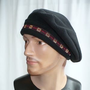 May include: A black fleece beret with a red and gold patterned band. The beret is worn on a mannequin's head.