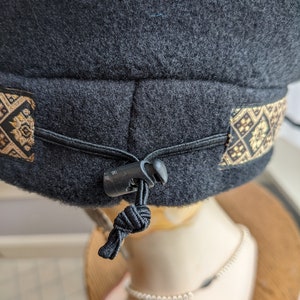Puede incluir: Sombrero de forro polar negro con una banda estampada en oro y negro y una correa ajustable negra con una hebilla de pl&aacute;stico.