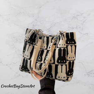 May include: A black and white tote bag with a repeating bunny pattern. The bag has cream-colored handles and silver chain accents. The text "CrochetBagStoreArt" is visible at the bottom left.
