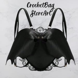 May include: Black bat-wing shaped backpack with adjustable straps. The backpack features a decorative lace trim and metal hardware. The text "CrochetBag StoreArt" is written in black script at the top of the image.
