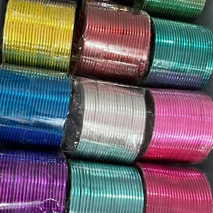May include: A collection of twelve sets of thin, metallic bangles in various vibrant colours including blue, yellow, red, green, silver, pink, and purple. Each set is individually wrapped in clear plastic and arranged in a grid pattern.