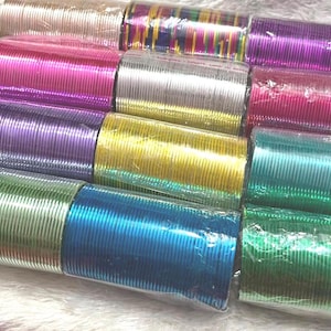Op de afbeelding: Een verzameling dunne metalen armbanden gerangschikt in meerdere stapels. De armbanden hebben verschillende metallic afwerkingen, waaronder zilver, goud, roze, paars, blauw, groen en een meerkleurig gestreept patroon, allemaal verpakt in doorzichtig plastic.