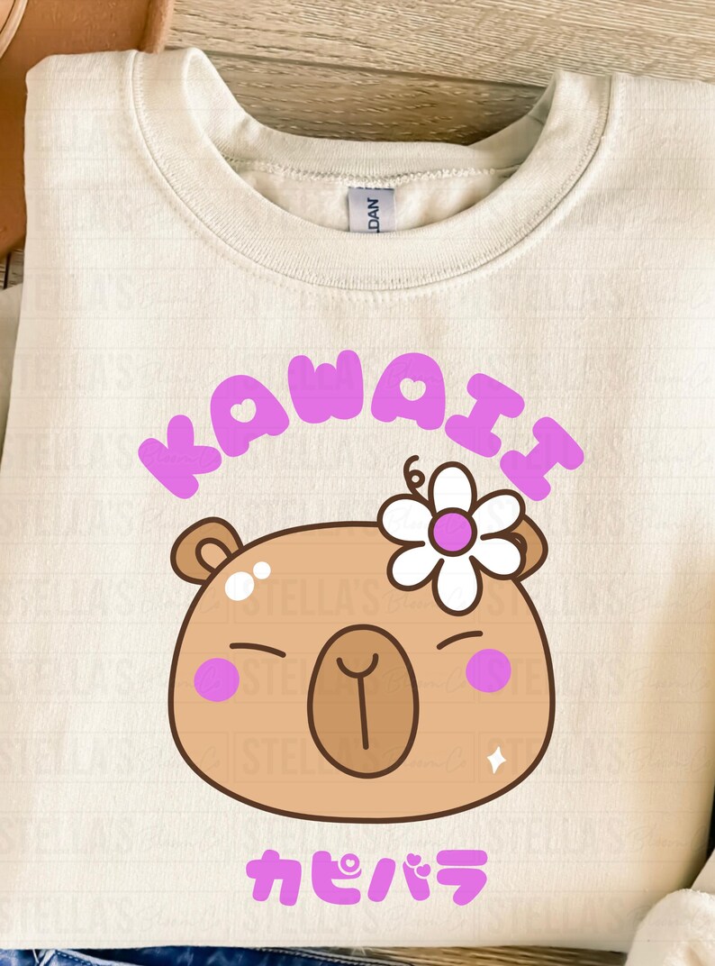 May include: Cream-colored sweatshirt with a Kawaii capybara graphic. The design features a brown capybara face with a flower, pink cheeks, and the word "KAWAII" in purple. The Japanese word "カピバラ" is below the capybara.