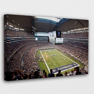 May include: Canvas print of a packed football stadium, featuring a green field with white yard lines and the word "COWBOYS" in blue. The stands are filled with spectators, and large screens hang from the ceiling.