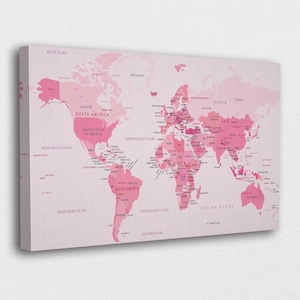 Puede incluir: Una impresión en lienzo de un mapa del mundo rosa. El mapa muestra los continentes y países en diferentes tonos de rosa, con nombres de países y etiquetas de océanos en una fuente rosa más oscura. El lienzo está montado en un marco de madera.