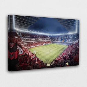 May include: Canvas print of a soccer stadium filled with fans. The field is green, and the stands are packed with people wearing red and white. The stadium is lit up with bright lights.