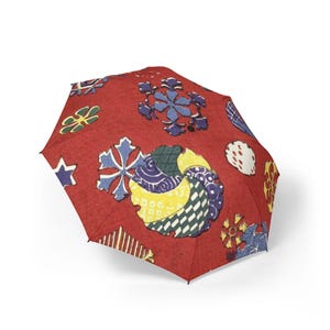 Pode incluir: Um guarda-chuva vermelho com um padrão repetitivo de várias formas, incluindo flocos de neve azuis, motivos circulares amarelos e azuis com detalhes texturizados e pequenos círculos brancos. A copa apresenta um design gráfico colorido.