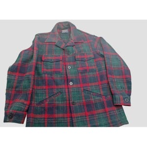 May include: A vintage plaid shirt in a classic pattern of red, green, and navy blue. The shirt features a collared neckline, button-down front, two chest pockets, and two lower pockets. The shirt is a medium weight and appears to be made of wool.