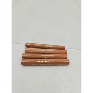 May include: Four cylindrical Mary Kay eye defining pencils with a light brown wood-grain finish. Each pencil features gold-colored text printed on the side, including the brand name, product type, and a net weight of .01 oz.