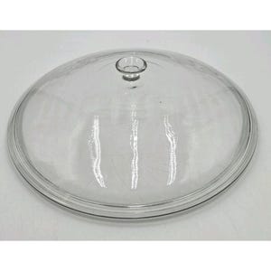 May include: A clear, round glass lid with a small, circular handle. The lid has a slightly domed shape and a thin, raised rim. The glass is transparent, allowing a clear view of the contents below. This kitchenware item is designed to fit over a pot or pan.