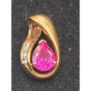 May include: A gold pendant featuring a pear-shaped, vibrant pink gemstone set in the center. The pendant has a smooth, curved gold frame that wraps around the stone, accented by three small, clear, round-cut stones set along the side.