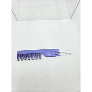May include: A lavender-colored hair highlighting comb with a dual design. One side features fine teeth, while the other has three metal prongs. The comb is made of plastic and is designed for hair styling and highlighting.