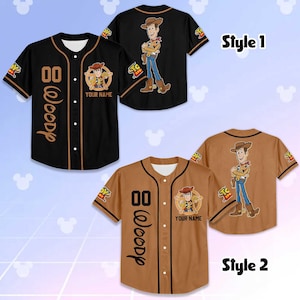 Puede incluir: Dos camisetas de b&eacute;isbol con el personaje Woody de Toy Story. Una es negra con detalles marrones, la otra es marr&oacute;n con detalles negros. Ambas tienen gr&aacute;ficos de Woody, el n&uacute;mero "00" y el nombre "Woody".