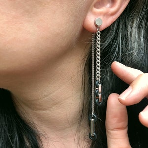 May include: Silver chain earrings with black rubber accents. The earrings are long and dangle from the earlobe.