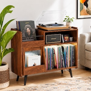 May include: A wooden record player stand with a built-in record storage compartment. The stand features a turntable, a Marshall speaker, and a collection of vinyl records. The stand is made of dark wood and has black legs. A potted plant is on the left.