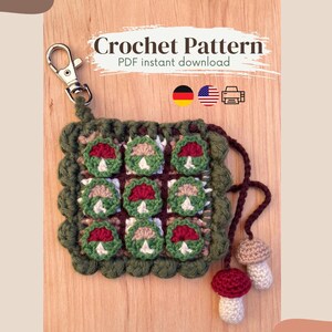 May include: A handmade crochet pattern featuring a square design with nine mushroom motifs in red, green, and white. The pattern includes a metal clasp and two small mushroom charms. The text "Crochet Pattern PDF instant download" is visible.
