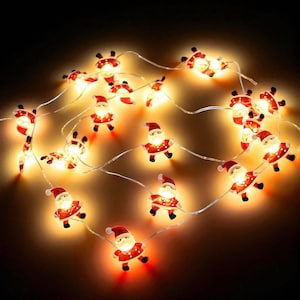 Puede incluir: Una cadena de luces navideñas con pequeñas figuras iluminadas de Papá Noel. Cada Papá Noel viste un traje y gorro rojos, con barba blanca y rostro sonriente. Las luces están en un cable transparente y delgado, para las fiestas.