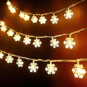Puede incluir: Cadena de luces LED blancas cálidas con forma de copo de nieve. Las luces están espaciadas uniformemente en un cable transparente. Los copos de nieve iluminados crean un ambiente festivo, ideal para decoraciones navideñas o de invierno.