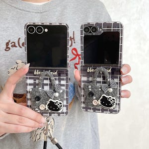 May include: Two clear phone cases with a black and white plaid pattern. Each case features a grey felt handbag design with a bow, pearl, and a Hello Kitty face. The text "black plaid" is visible.