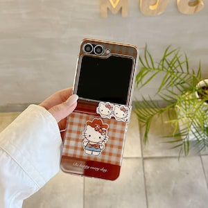 Op de afbeelding: Transparante telefoonhoes met een rood-bruin ruitpatroon en Hello Kitty-afbeeldingen. De hoes heeft een scharnierend ontwerp en bevat de tekst "Be happy every day."