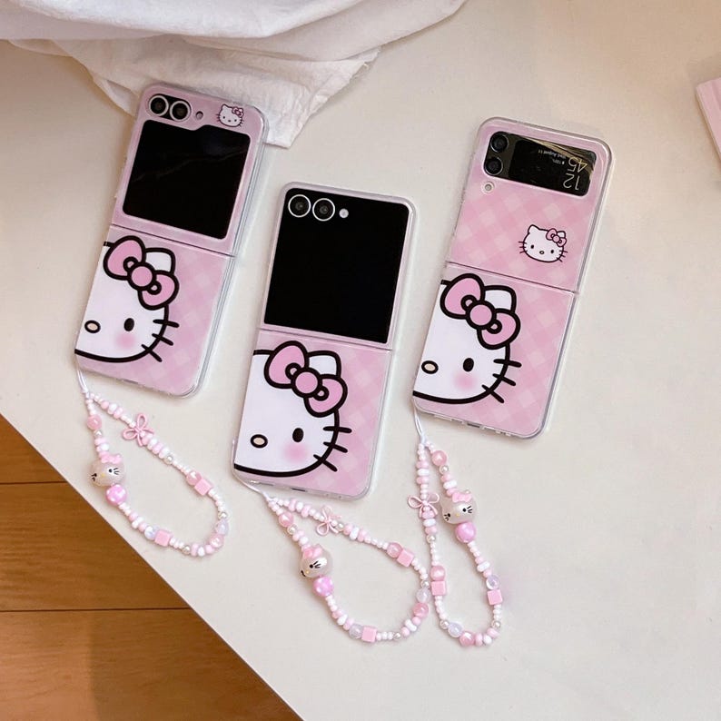 May include: Pink foldable phone cases featuring a Hello Kitty design. The cases have a pink and white checked pattern. Each case is paired with a beaded wrist strap, adorned with Hello Kitty charms.