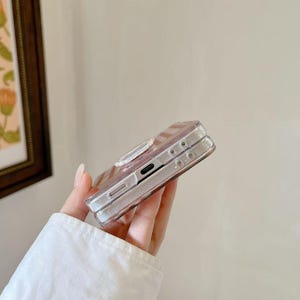 Op de afbeelding: Een doorzichtige telefoonhoes met een roze en wit gestreept ontwerp. De hoes heeft een ingebouwde ringhouder en is gemaakt van transparant materiaal. De telefoonhoes is ontworpen om de telefoon te beschermen.