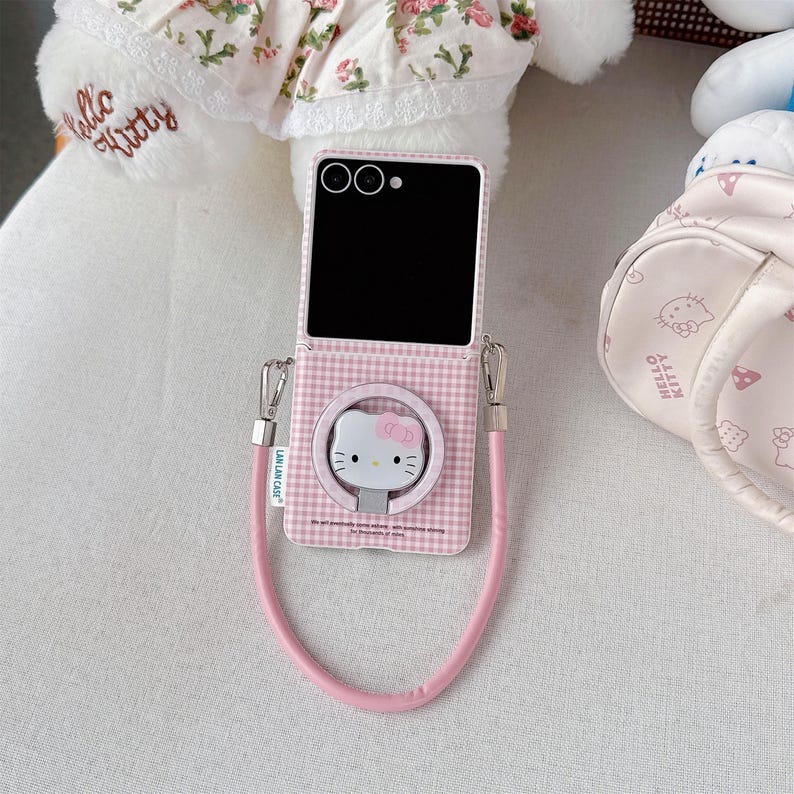 May include: A pink and white checked phone case with a Hello Kitty design. It has a matching pink strap and silver-coloured metal hardware. The phone case is open, showing the phone's screen and camera.