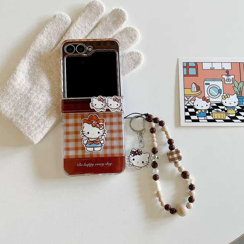 Op de afbeelding: Een doorzichtige telefoonhoes met een bruin en wit geruit patroon met een Hello Kitty-afbeelding. De hoes heeft een bijpassende sleutelhanger met een kralenband. Er is ook een kleine kaart met een Hello Kitty-illustratie.